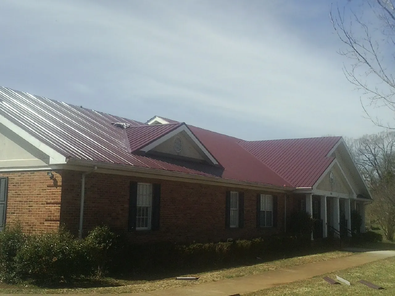 Red metal roof with gabled entries on a long brick building, from a Hail Damage Roof Repair job in Bossier City