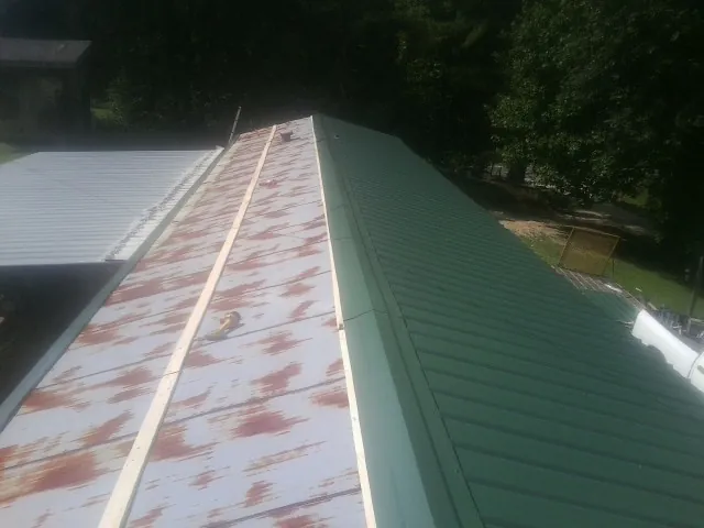 Old rusted panels beside newly installed green metal roofing — Wind Damage Roof Repair by Roofing Brothers in Bossier City