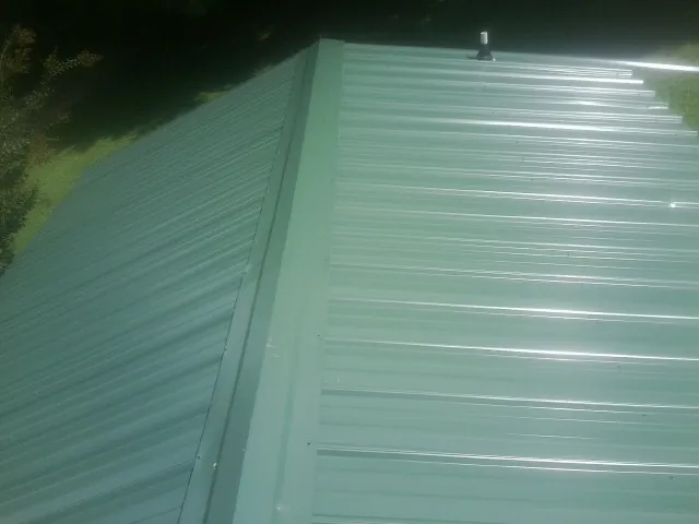 New green metal panels meeting at the ridge of a roof — Flat Roof Repair work by our crew in Bossier City