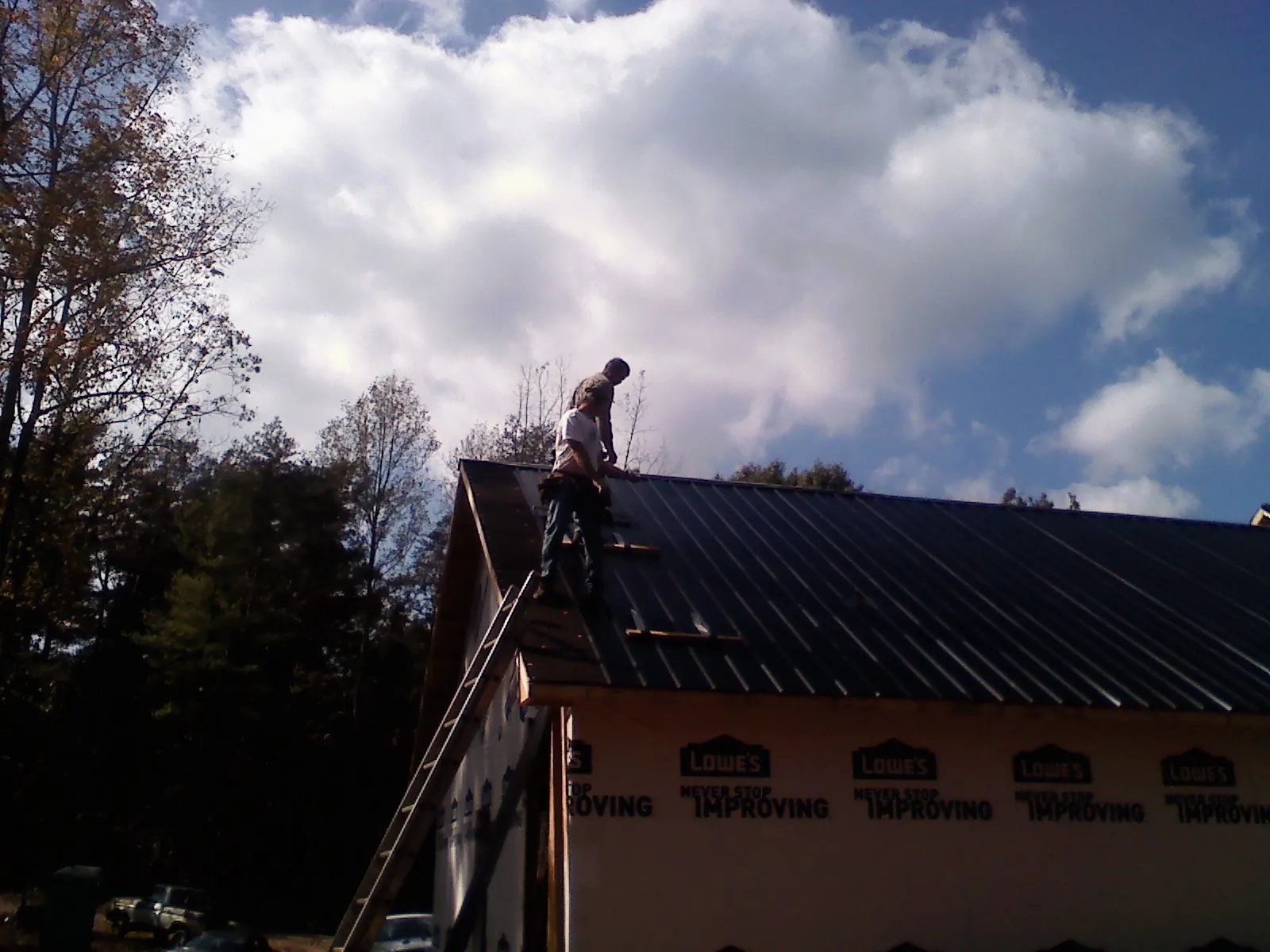 Roofer fastening dark metal panels high against a cloudy sky, from a Roof Inspection job in Bossier City