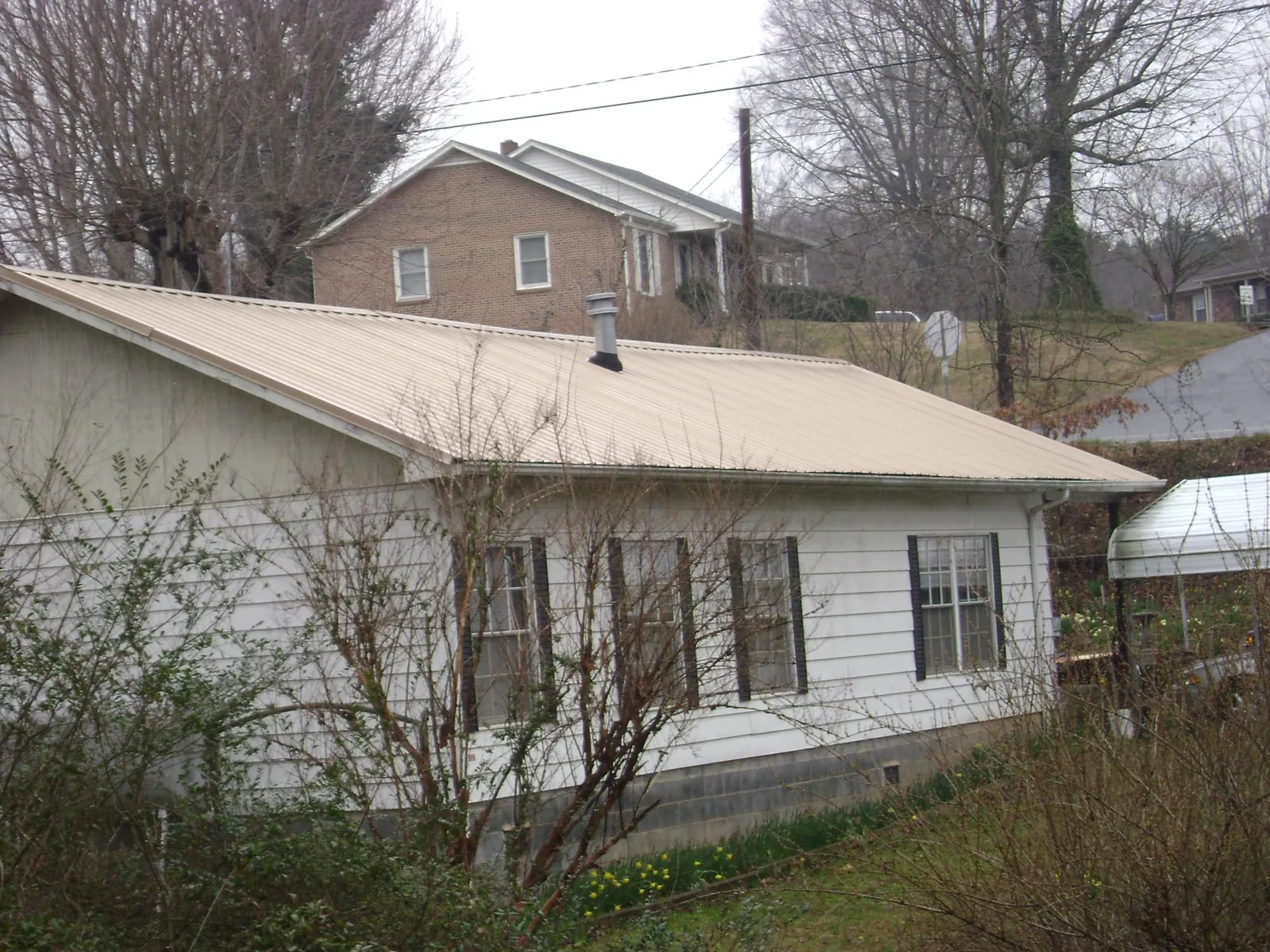 Tan metal roof on a white sided house set into a hillside — Commercial Roofing by Roofing Brothers in Bossier City