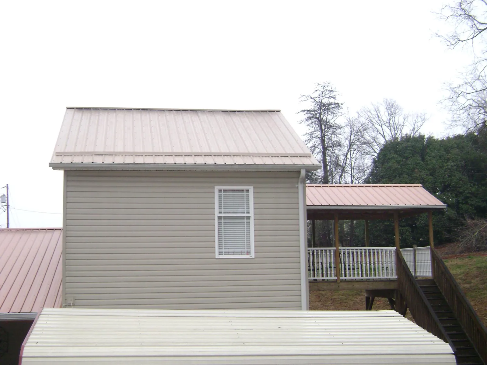 Tan metal roofs on a two story addition and attached porch, from a Roof Replacement job in Bossier City